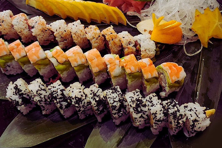 platter of sushi rolls with lemon slices, wasabi, gari, and starfruit