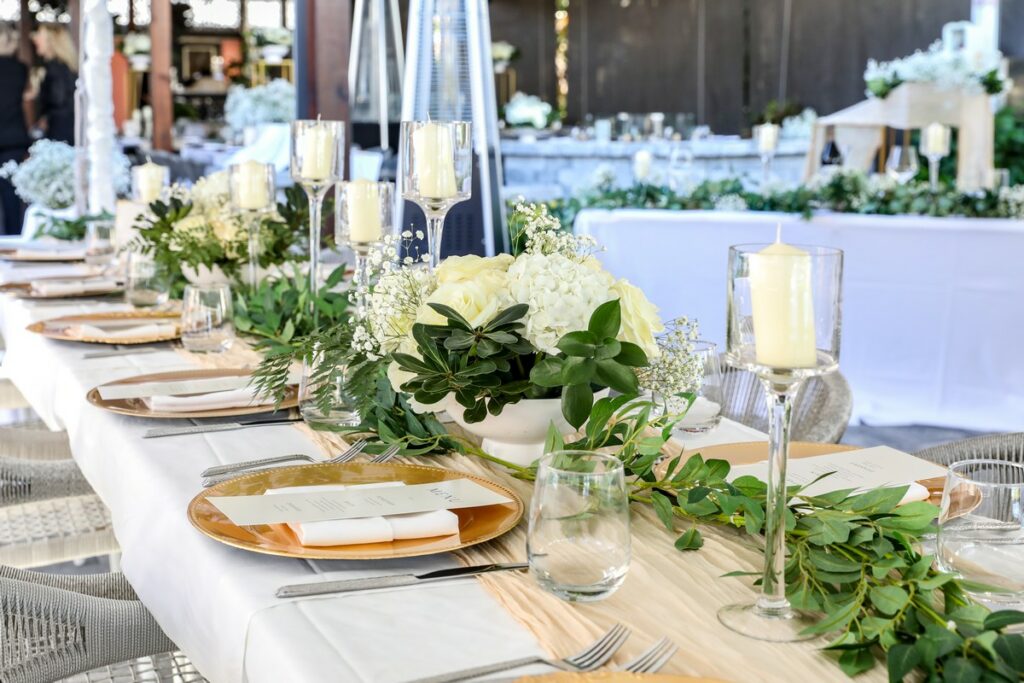 bowls with white flowers and tall candles decorate a table at a wedding reception