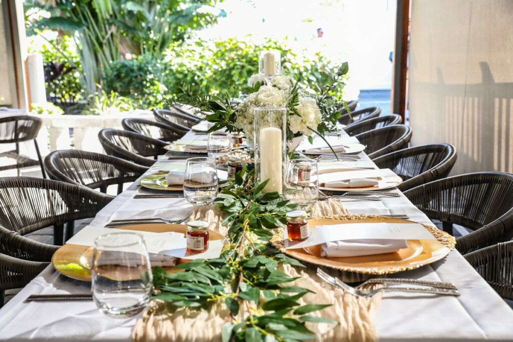 long table decorated with floral arrangements, foliage, and gold place settings for a wedding reception at Magnolias on the Bay