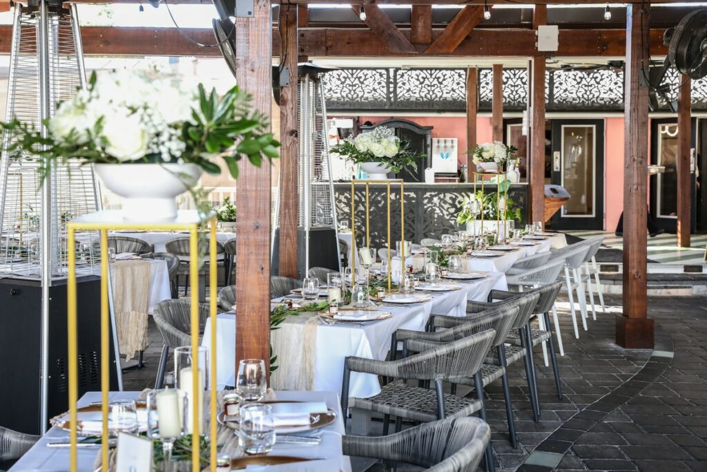 a row of tables decorated for a wedding under a covered patio at Magnolias on the Bay